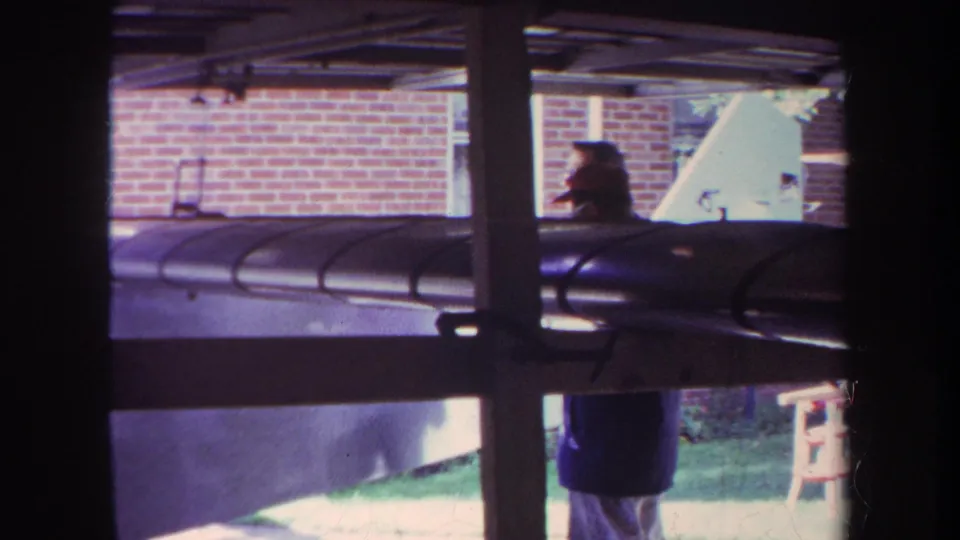 1969 Volmer Yucaipa frame with a person beside the large wooden model airplane, seen through posts and beams near a brick building.