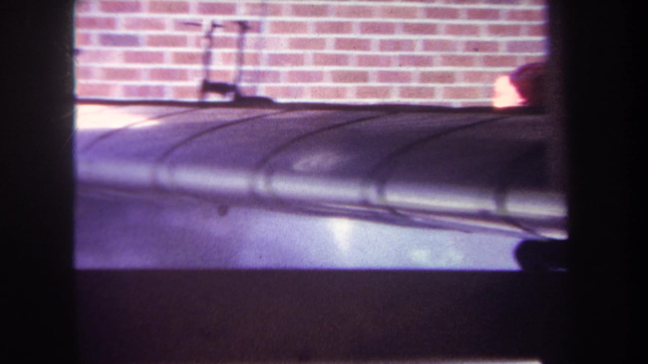 1969 Yucaipa home-movie frame showing a silver model airplane body with dark framing in front of a brick wall.