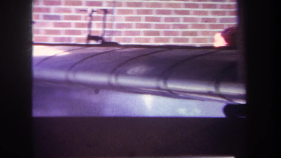 1969 Yucaipa home-movie frame showing a silver model airplane body with dark framing in front of a brick wall.
