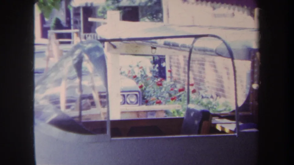 1969 Yucaipa frame showing a clear model airplane canopy with red flowers, brickwork, and outdoor furniture in the background.