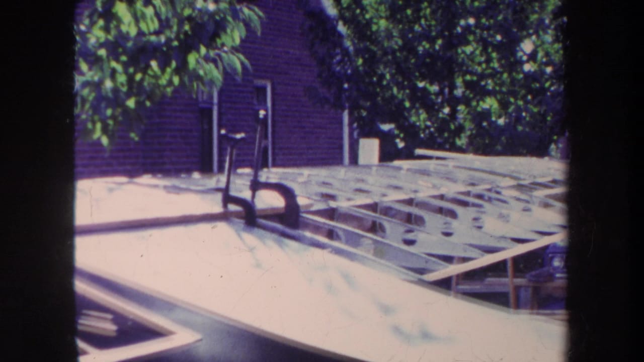 Wooden aircraft frame and pale wing section in a sunny residential yard.