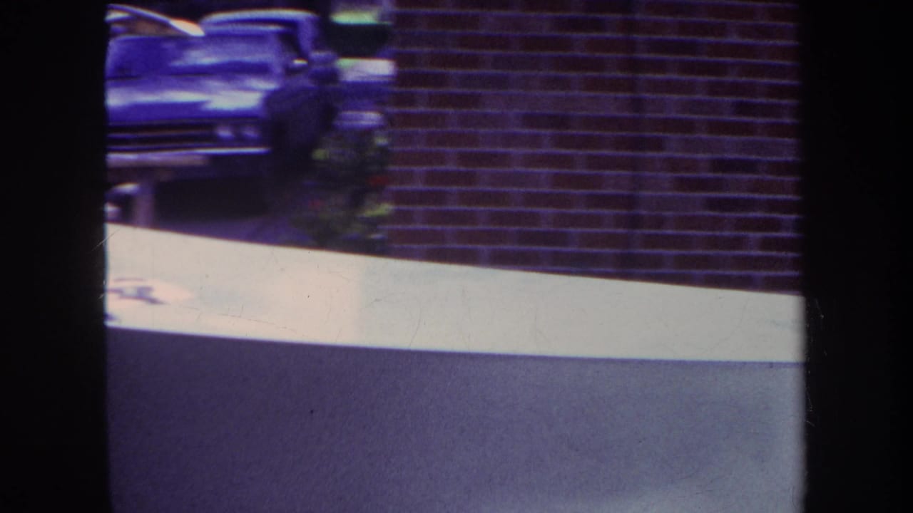 1969 Yucaipa-area 8mm frame showing the edge of a pale skateboard ramp against a red brick building, with a partial car visible above.