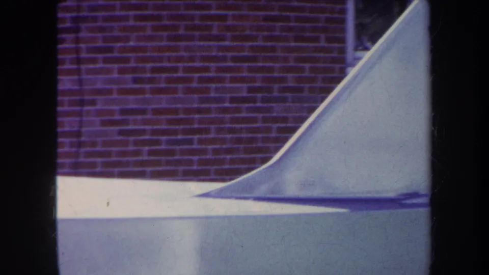 1969 Yucaipa-area 8mm frame with the curved end of a pale skateboard ramp set against a red brick exterior wall.