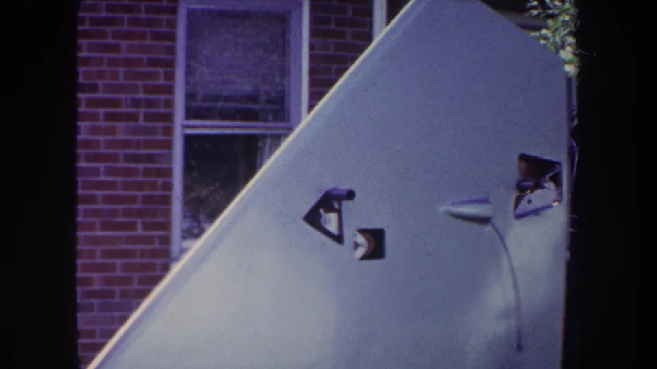 1969 Yucaipa-area 8mm frame showing a pale skateboard ramp with small markings, brick wall, windows, and film gate edges.