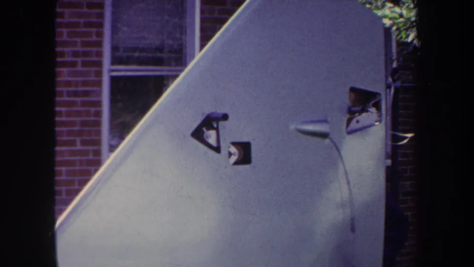 Final 1969 Yucaipa frame keeps the pale aircraft tail and markings in view against the brick residential background.