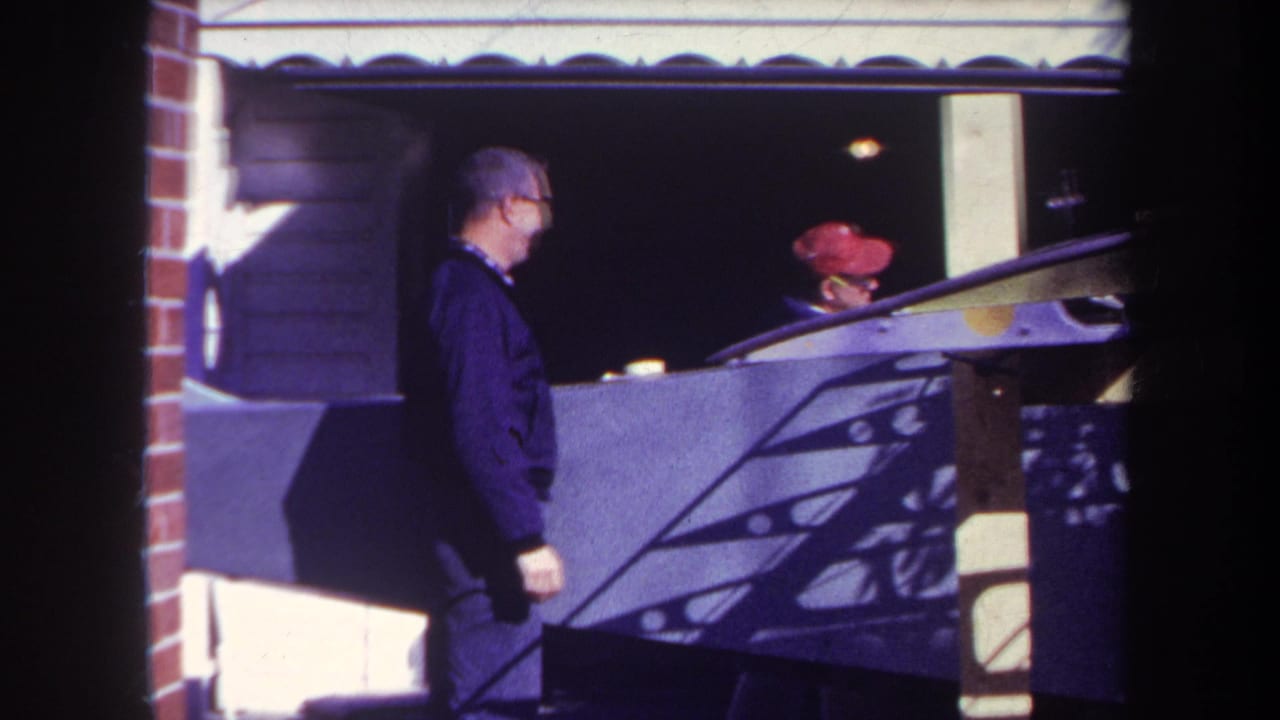 1969 Yucaipa home-movie frame showing an adult man near a fairground booth and another man behind the counter in bright sun.