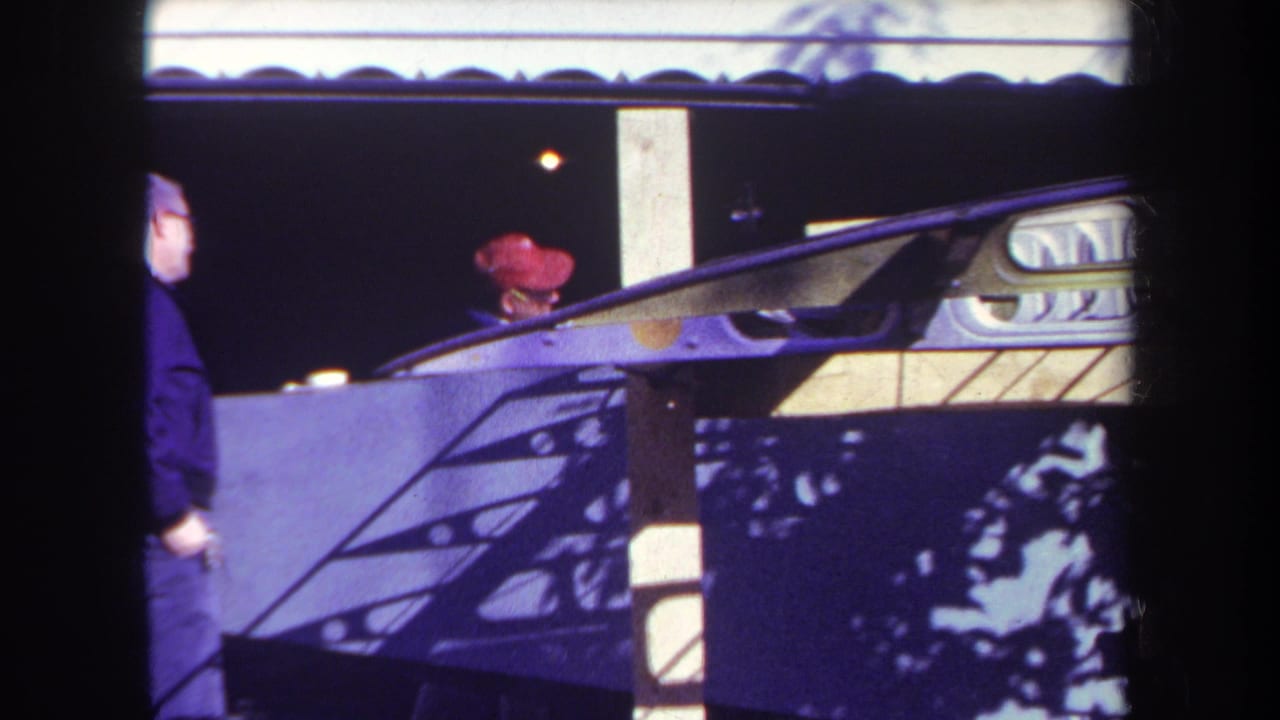 Man passes partly out of frame near a booth while the red-capped man remains behind the counter.