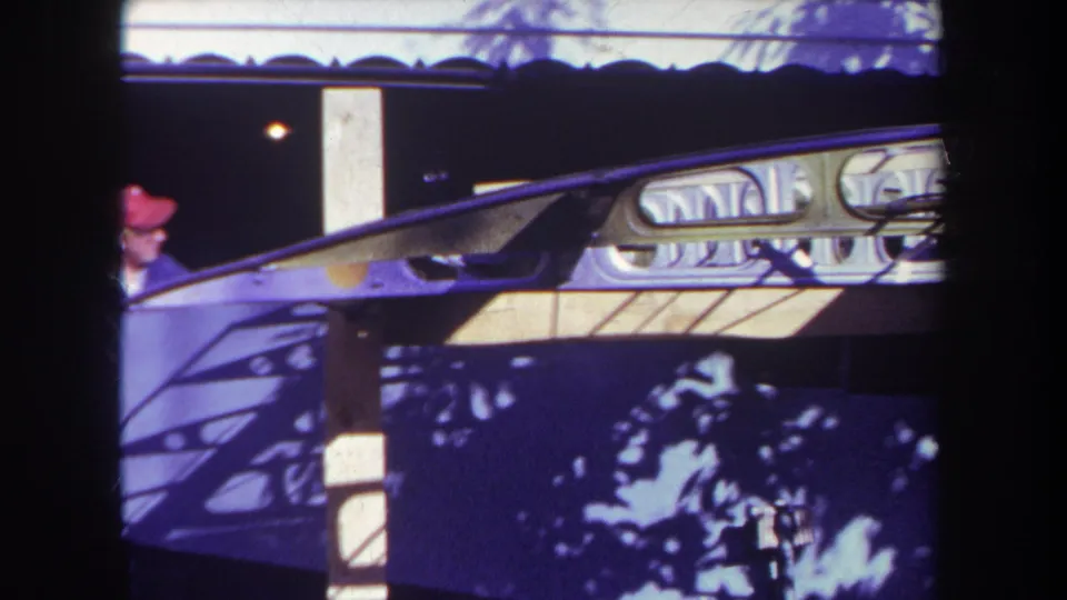 1969 Yucaipa home-movie frame with a red-capped adult behind a booth, decorative trim, and strong blue-purple film shadows.
