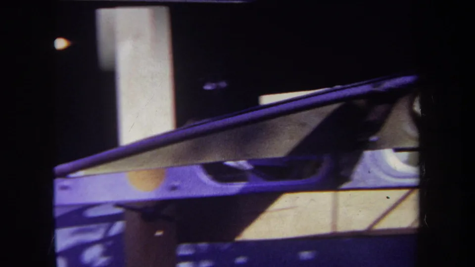 1969 Volmer Yucaipa 8mm frame showing a lower section of the unidentified apparatus with angled rails, supports, and strong shadows.