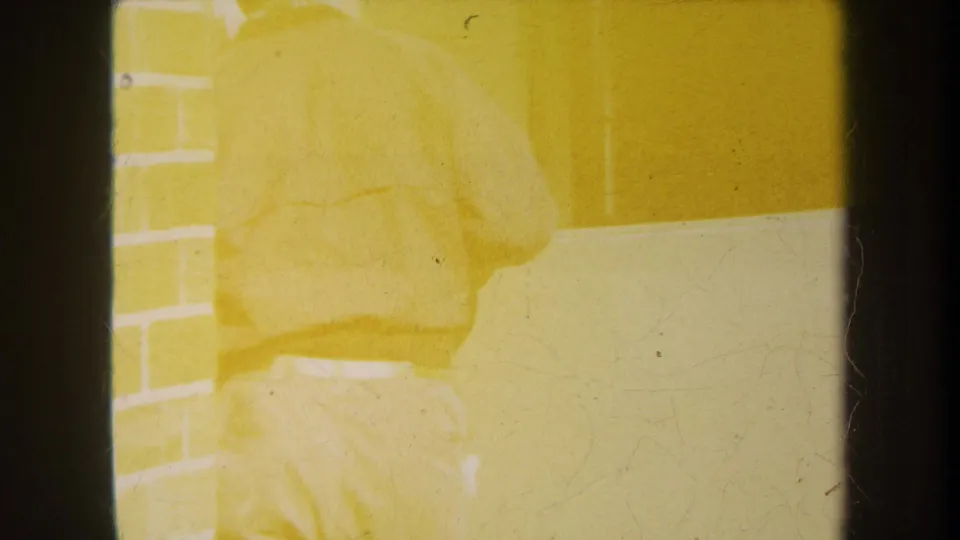 Overexposed 1969 home-movie frame in Yucaipa showing a man partly obscured near brickwork and equipment, with yellow film color shift.