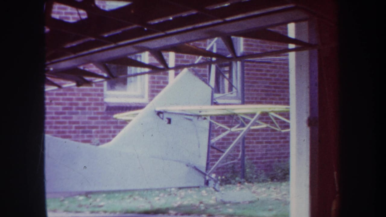 White airplane tail and struts beside a brick wall beneath dark roof beams.