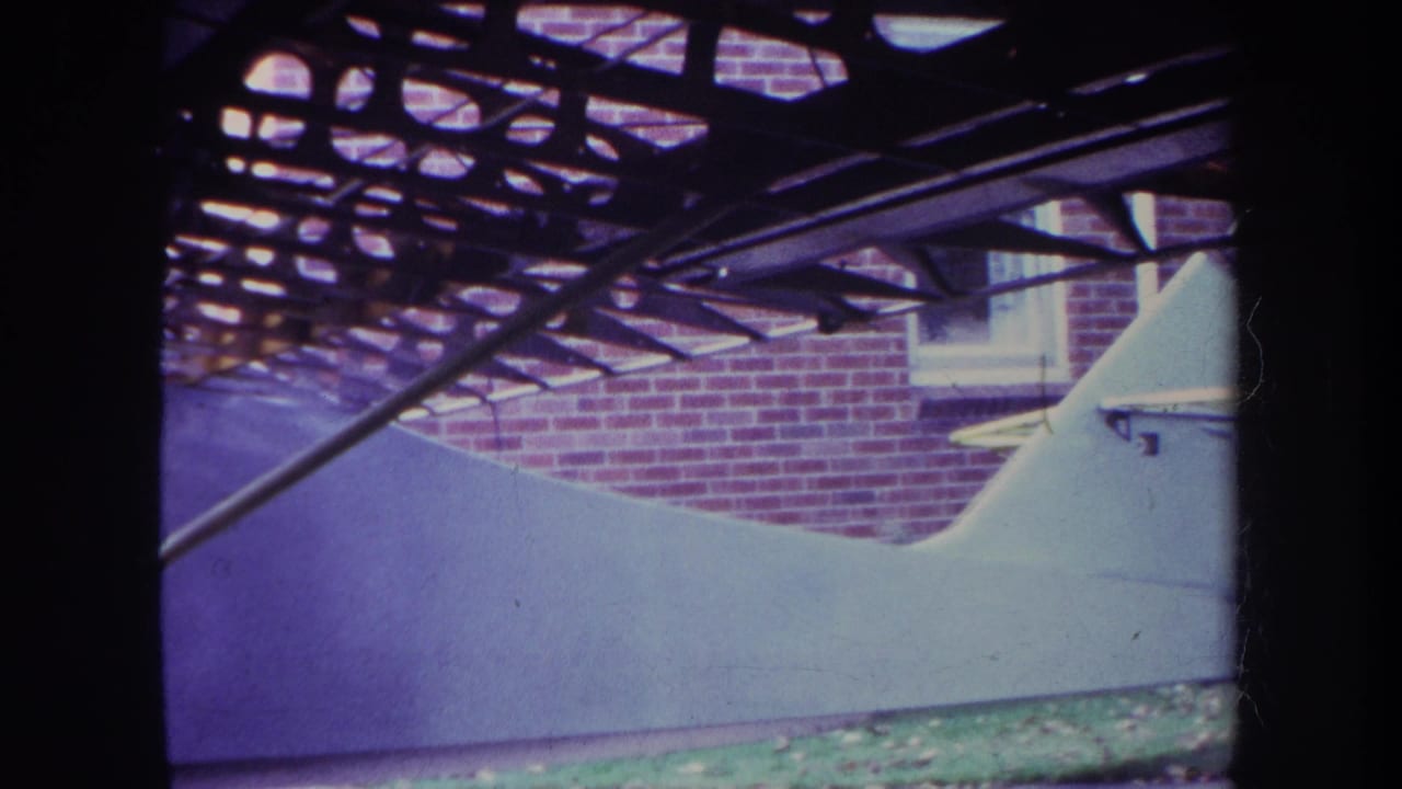 White unfinished aircraft fuselage beside a red brick wall and exposed overhead framework.