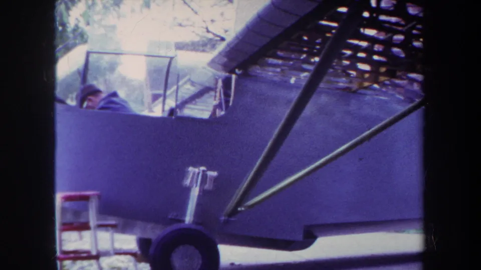 1969 Yucaipa frame of a light airplane beside a yard or residential area, with pilot visible in the cockpit and strong 8mm color shift.
