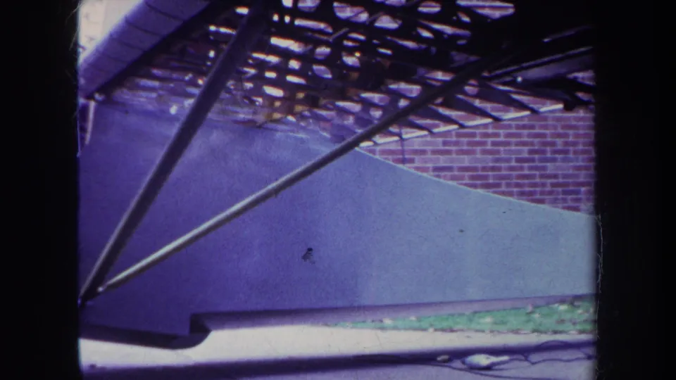 A tight 8mm frame shows the airplane struts crossing the fuselage, with the wing underside and brick wall behind it.