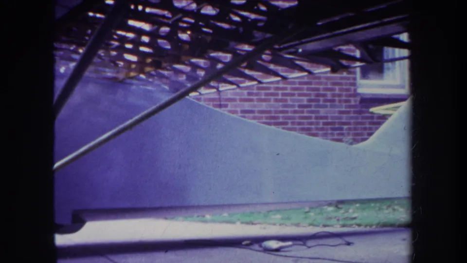 End frame of the 1969 Yucaipa clip shows the small airplane body and struts close to a brick building with a partial window.