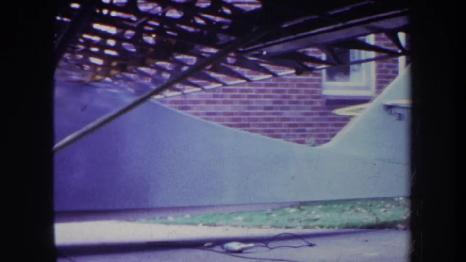 1969 Yucaipa home-movie frame showing a small white aircraft beside a brick house, seen through a dark foreground frame.