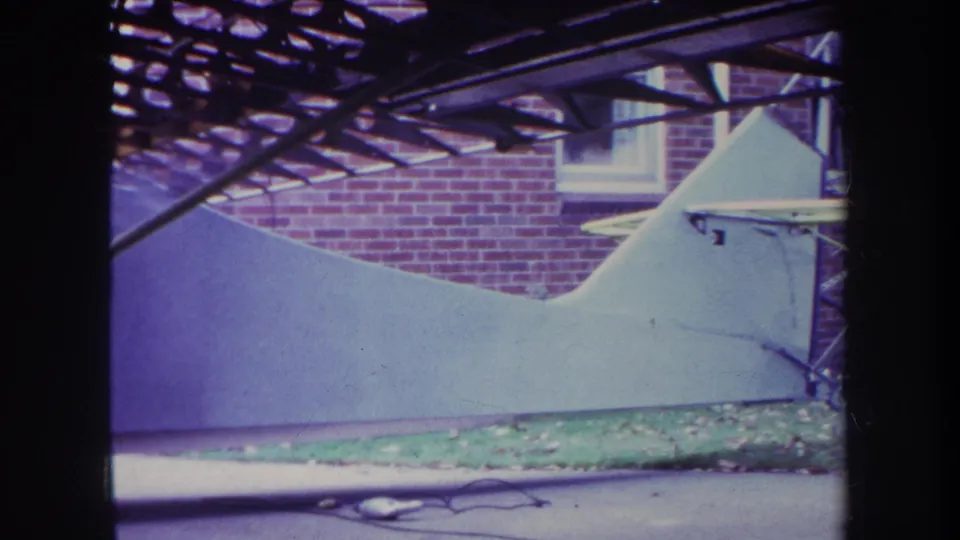1969 Yucaipa frame with the white aircraft body parked near a brick house and metal canopy, with lawn and pavement below.