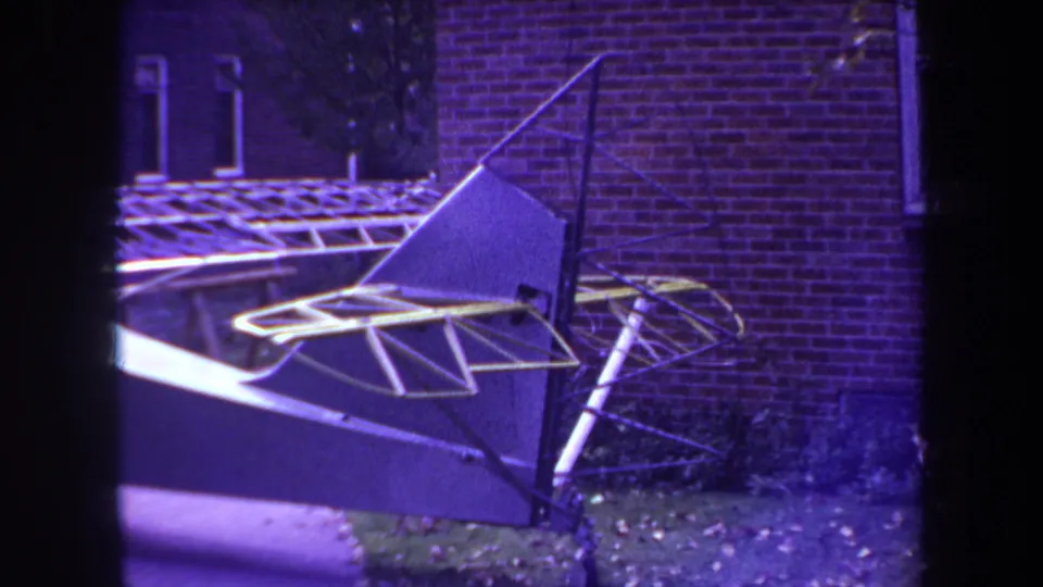 Purple-tinted 8mm frame of the homemade aircraft in the Yucaipa backyard setting, with brick wall and carport framing visible.