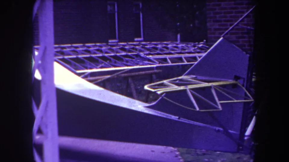 1969 Yucaipa footage frame showing the model airplane's tail framework cropped closely, with purple-tinted 8mm color.