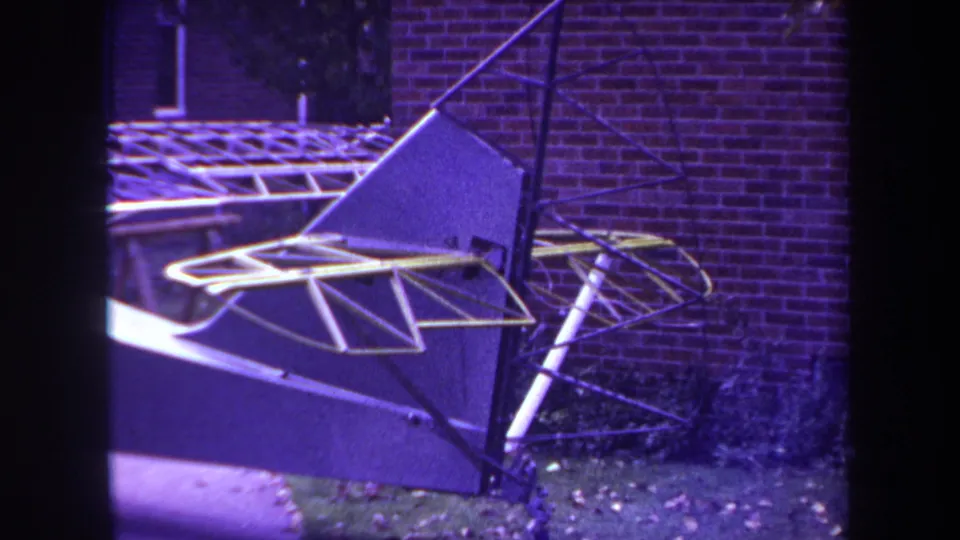 Home-movie footage from 1969 Yucaipa shows an unfinished aircraft frame with yellow tubing, dark fabric panels, and a brick wall behind it.