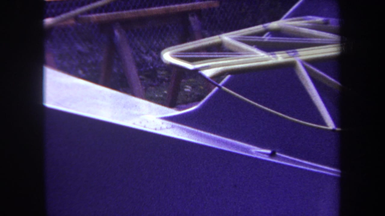 Close view of a metal rod framework over a purple-toned surface with fence and wood behind it.