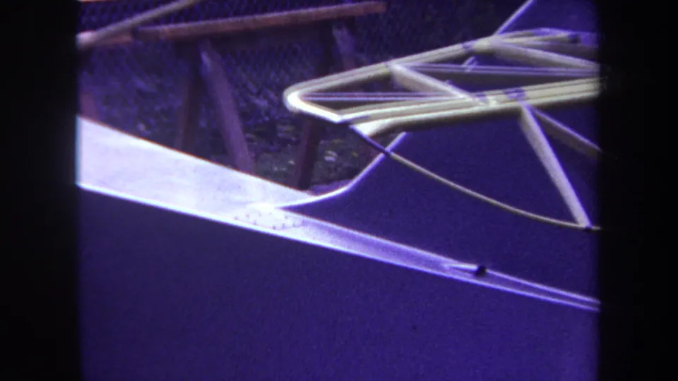 1969 Yucaipa-area 8mm frame showing a close-up metal framework with triangular rods, a purple cast, and fencing in the background.