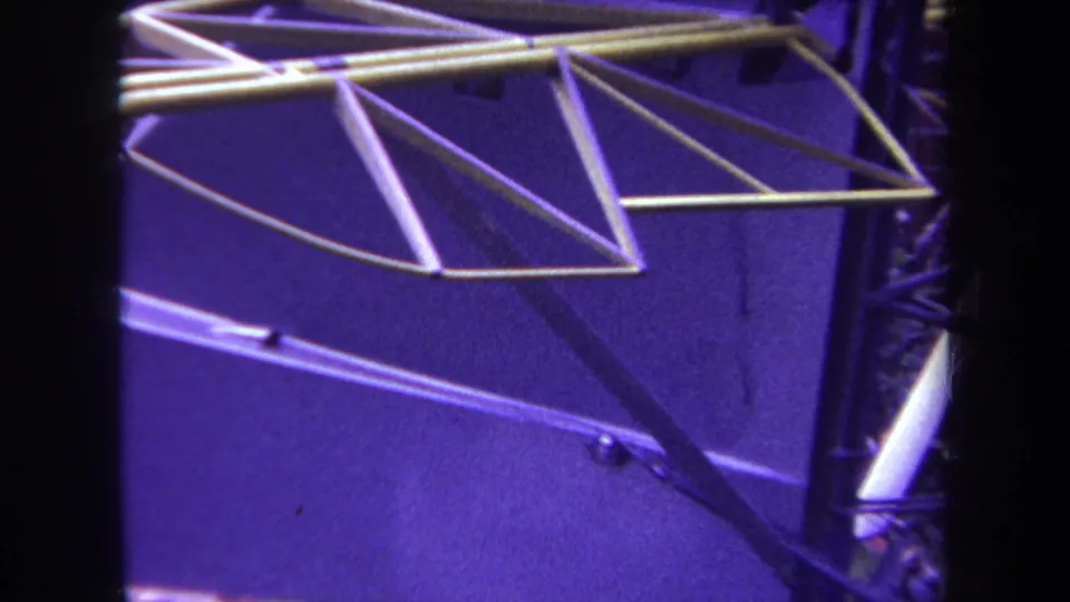 1969 Yucaipa-area 8mm frame showing the metal structure from a lower angle with support rods, grass, and leaves below.