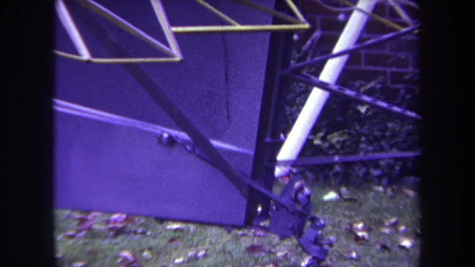 1969 Yucaipa-area 8mm frame showing metal supports beside a purple-toned surface, with grass and fallen leaves at the edge.
