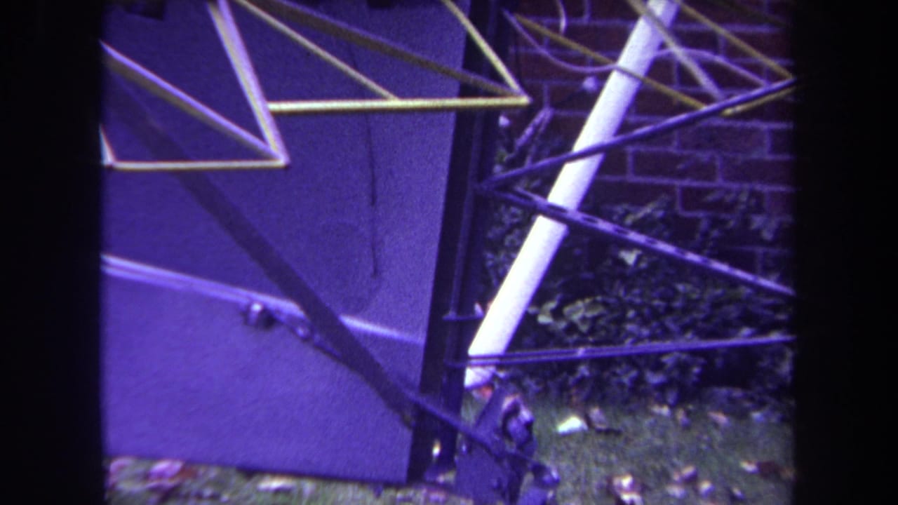 Close view of an open metal aircraft frame beside a brick wall and greenery.