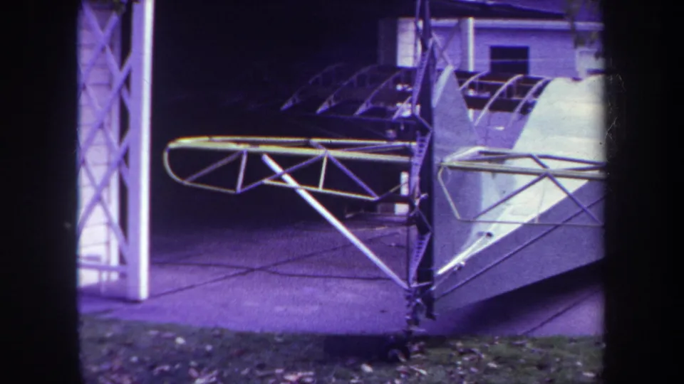 1969 Yucaipa home-movie view of a small white experimental aircraft with exposed truss wings in a driveway.