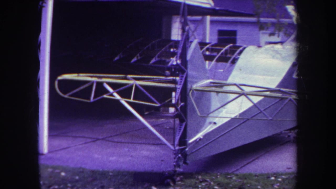 1969 Yucaipa home-movie frame showing a white homemade aircraft body with metal struts beside a house and driveway.