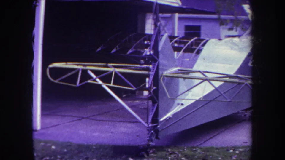 1969 Yucaipa home-movie frame showing a white homemade aircraft body with metal struts beside a house and driveway.