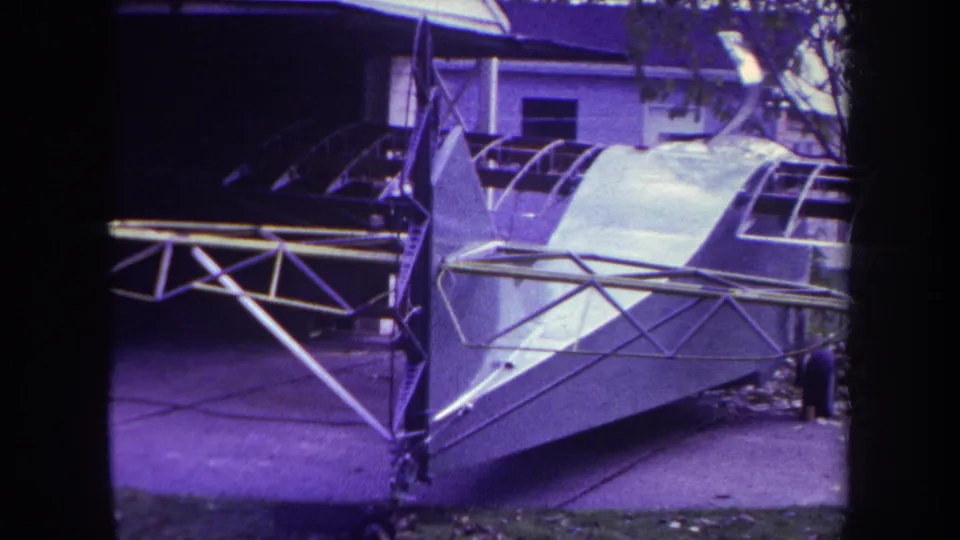 1969 Yucaipa frame with the homemade aircraft seen from the side, showing open framework, fuselage panels, and a residential backdrop.