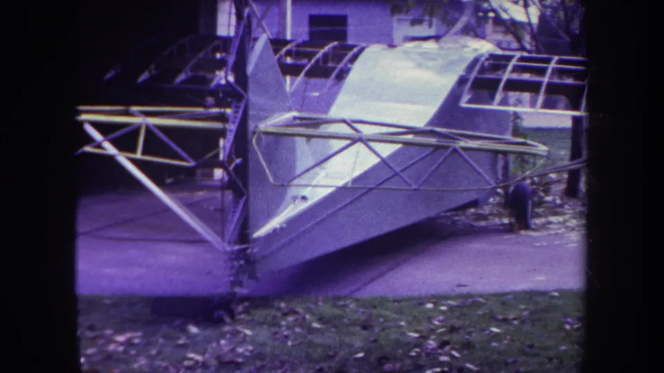 8mm frame from the Yucaipa clip showing the aircraft nose area, open framing, trees, and leaf-covered ground.