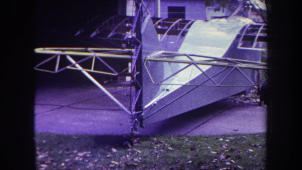 Unfinished small airplane fuselage and tail framework beside a driveway.