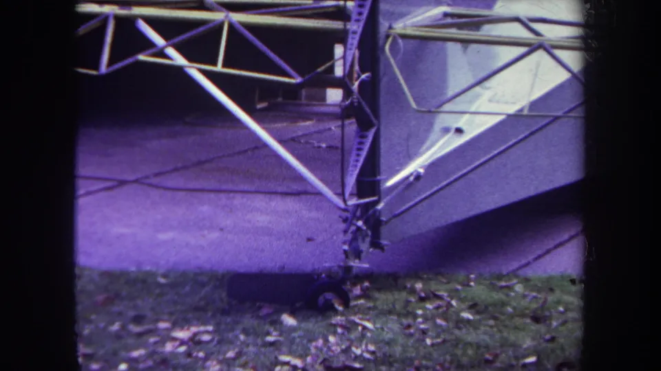 1969 Yucaipa frame with a closer view of the unfinished aircraft structure, including diagonal tubing, fuselage side, wheel assembly, driveway, and grass.
