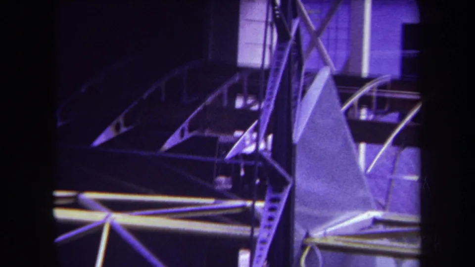 Purple-tinted 8mm frame showing a shadowed aircraft structure with curved tubing, braces, and angular tail components.