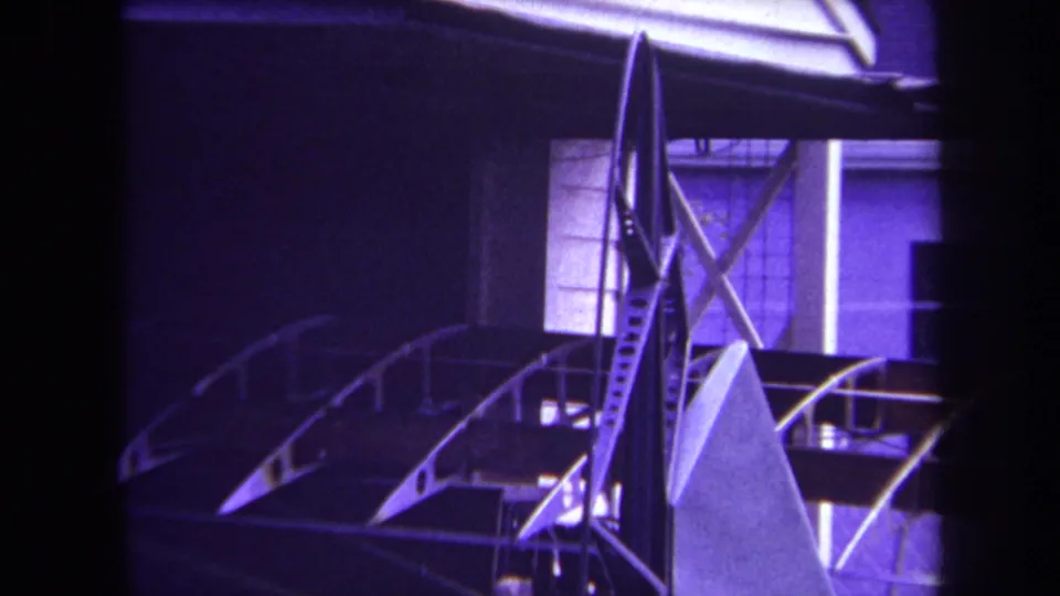 1969 Volmer Yucaipa 8mm still of airplane tail assembly, showing braces, curved frame pieces, and metal surfaces in aged color.