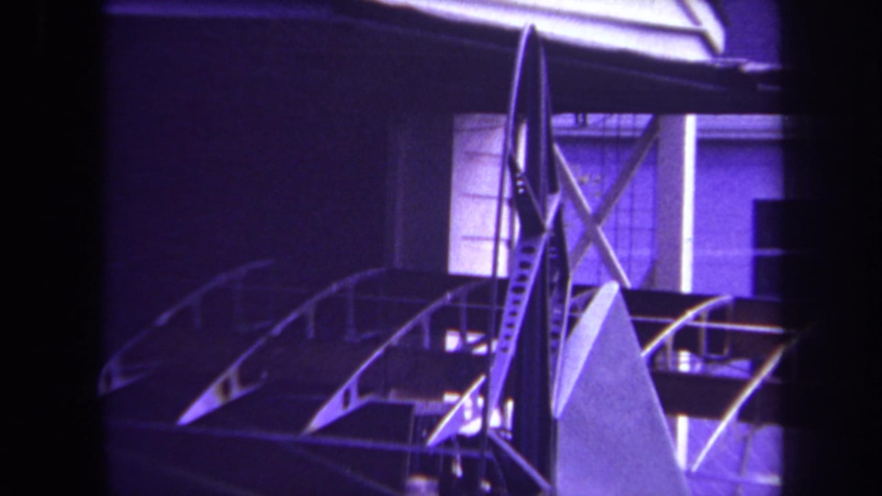 Unfinished small aircraft frame beside a house with dark film borders.