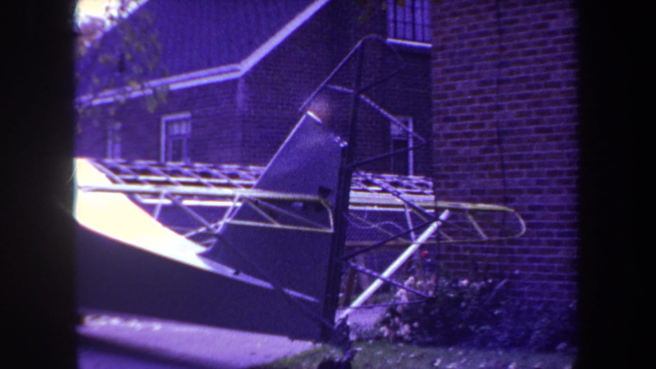 Close view of a small aircraft tail section beside a brick house.
