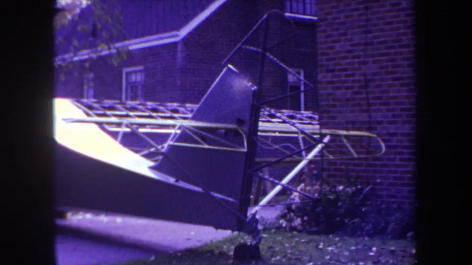 1969 Yucaipa frame with purple-shifted 8mm color, showing an aircraft tail assembly beside a brick house exterior.