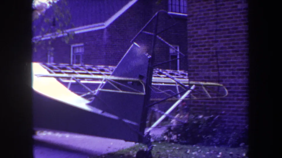 Close 8mm view of a small aircraft tail section near a brick house in Yucaipa, California, in 1969.