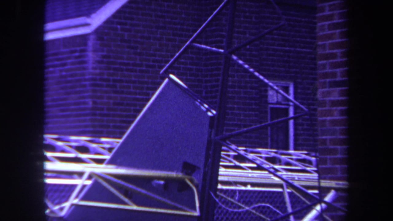 1969 Yucaipa 8mm frame showing an abstract metal sculpture against a brick exterior with windows and tubing.