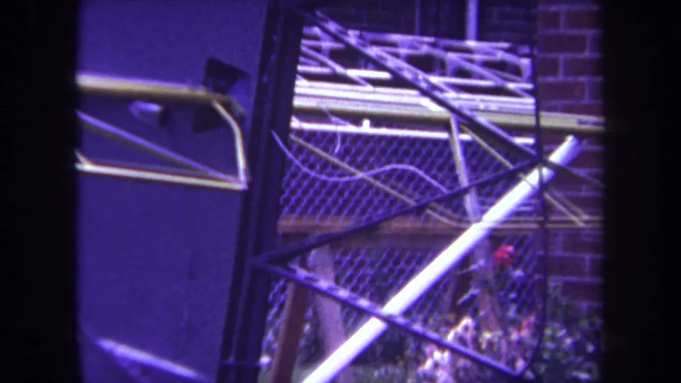 1969 Yucaipa 8mm frame showing a close view of metal sculpture framework, mesh, brickwork, and small plants.