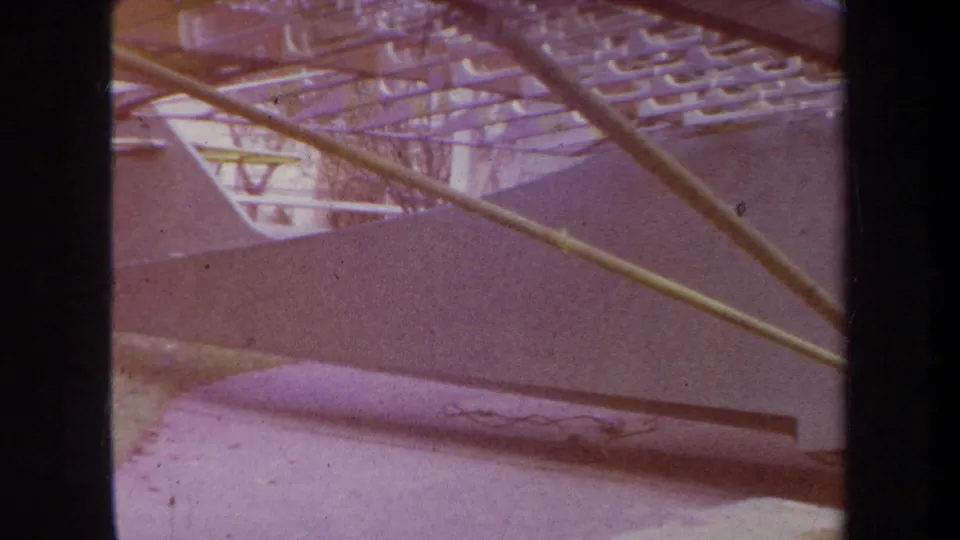 Close 1969 home-movie frame of the aircraft body and struts, tinted purple and brown by aged 8mm film color shift.