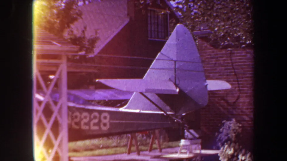 1969 Yucaipa frame showing the tail and rear side of the homemade aircraft, with the number 2228 visible on the fuselage near a brick wall.