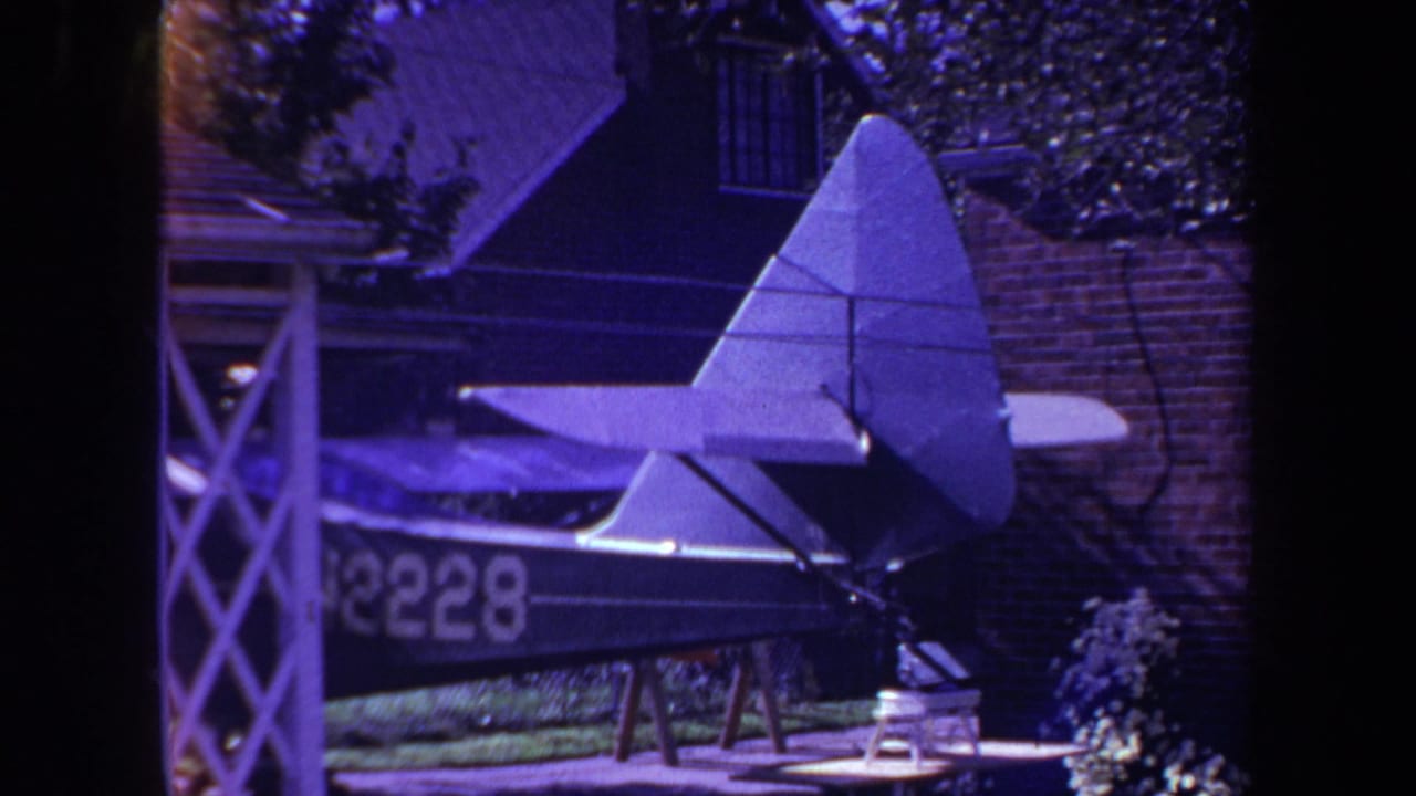 1969 8mm frame from Yucaipa showing a homemade model airplane on sawhorses in a residential backyard garden.