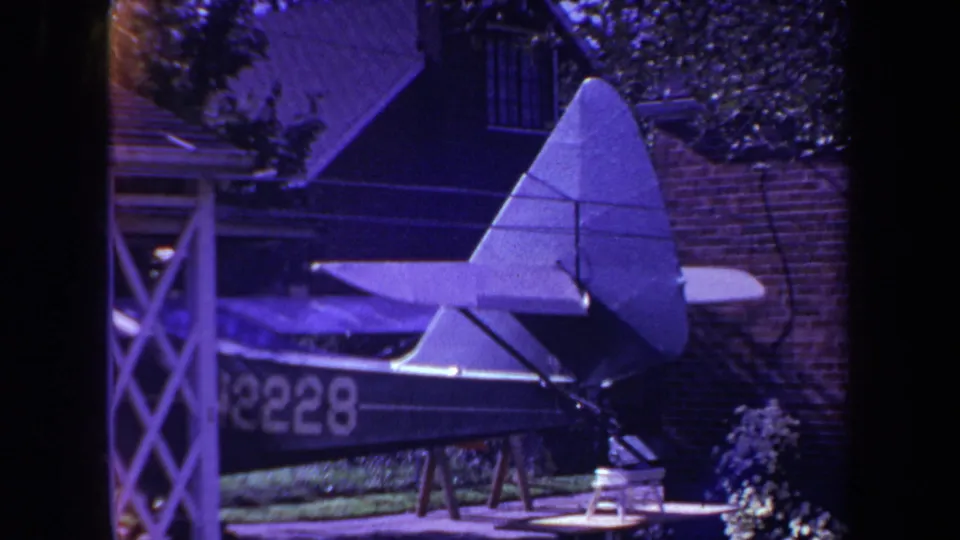 1969 8mm frame from Yucaipa showing a homemade model airplane on sawhorses in a residential backyard garden.