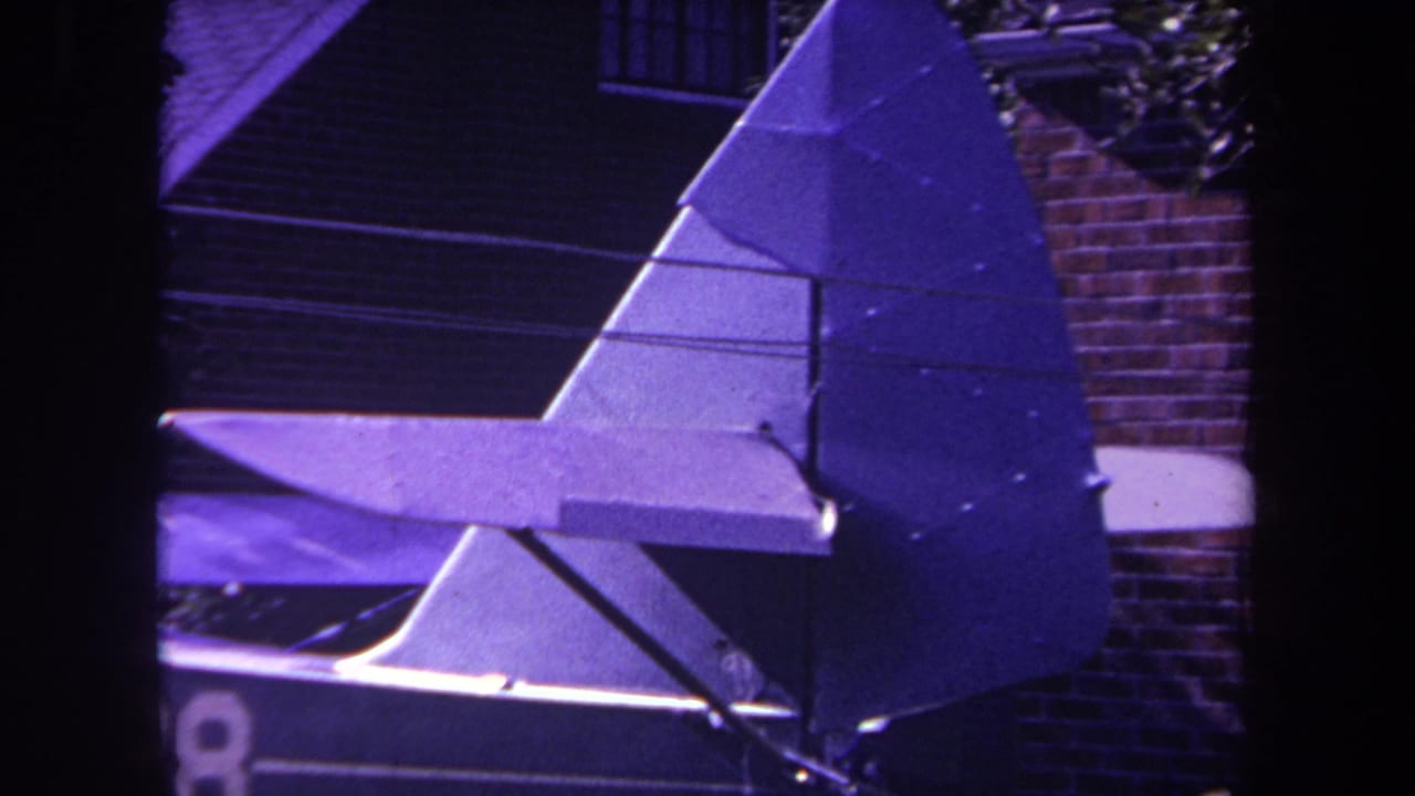 Airplane tail assembly with triangular rudder framed against brick and window details.
