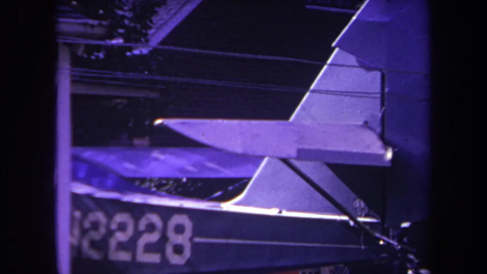 Final 1969 8mm frame from Yucaipa showing the aircraft's tail surfaces and a partial registration marking, with the house exterior still visible behind the plane.